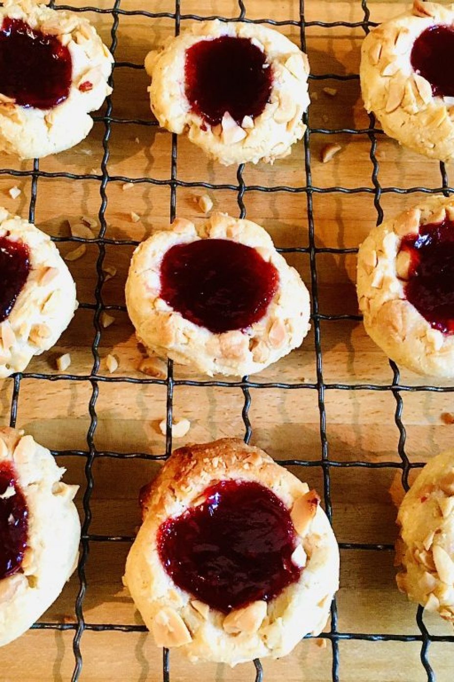 Rows of peanut butter and raspberry jam thumbprint cookies on a wire rack
