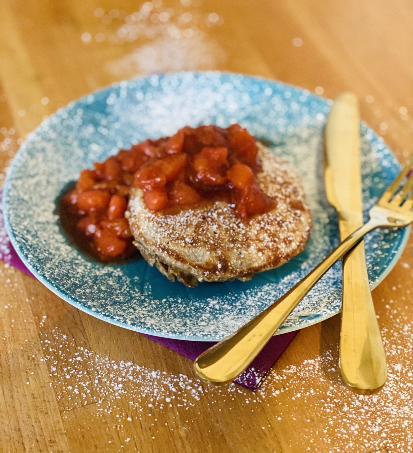 Stack of cinnamon oat pancakes served with spiced plums and a dusting of icing sugar