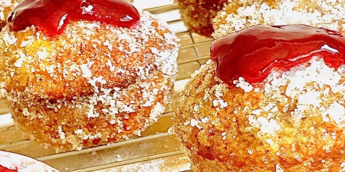 Jam donut muffins, coated in sugar and topped with raspberry jam on a cooling rack