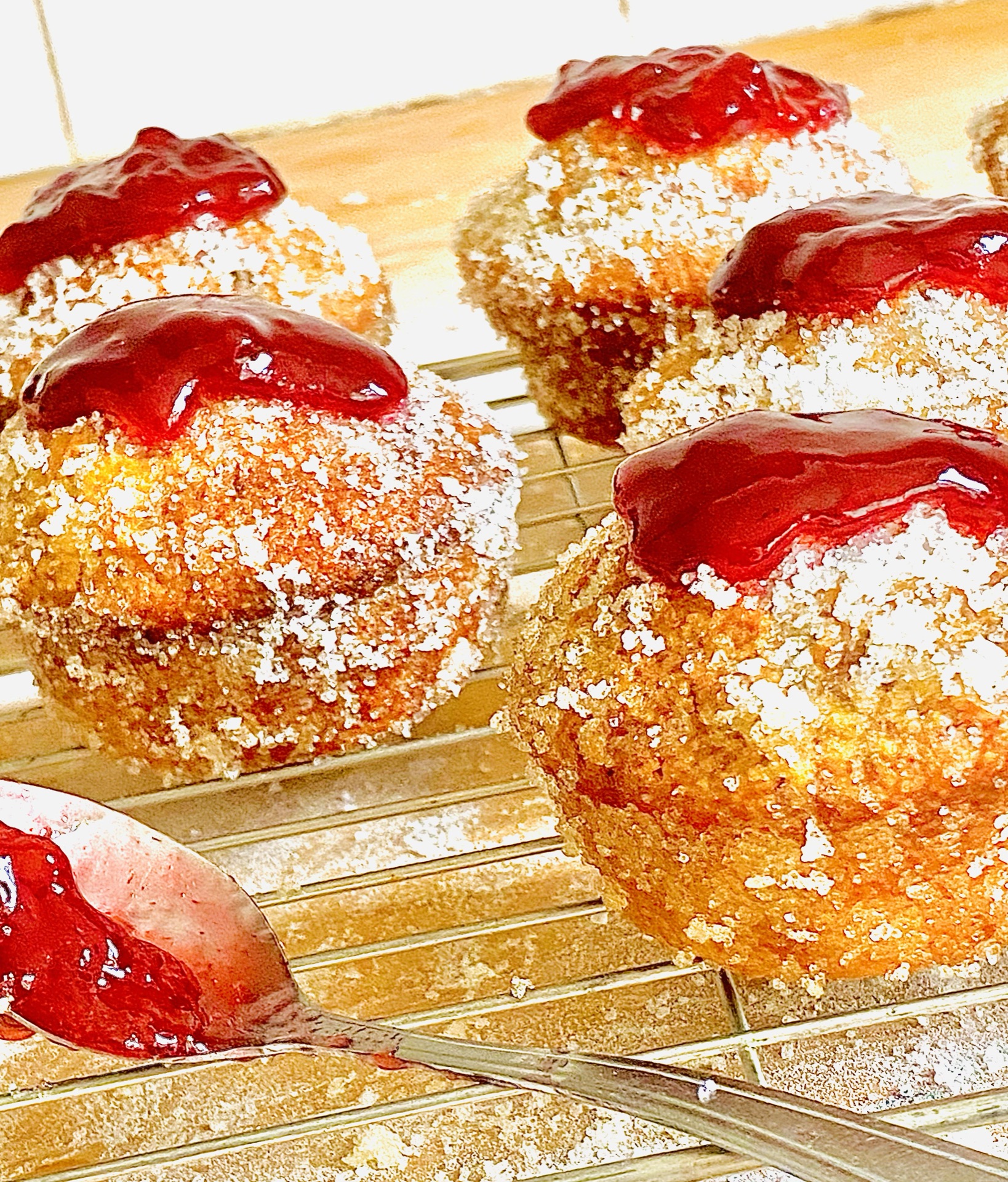 Jam donut muffins, coated in sugar and topped with raspberry jam on a cooling rack