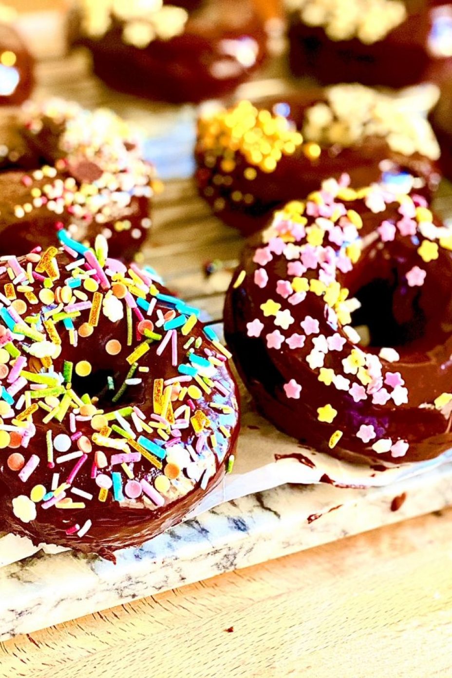 A row of double chocolate baked doughnuts, covered in a layer of chocolate ganache icing and covered with multicoloured sprinkles