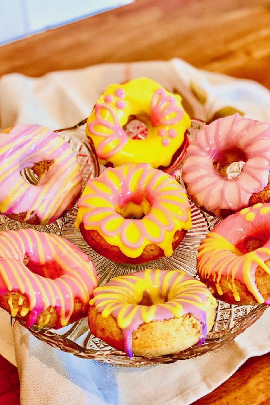 Baked doughnuts topped with coloured icing displayed on a cake stand