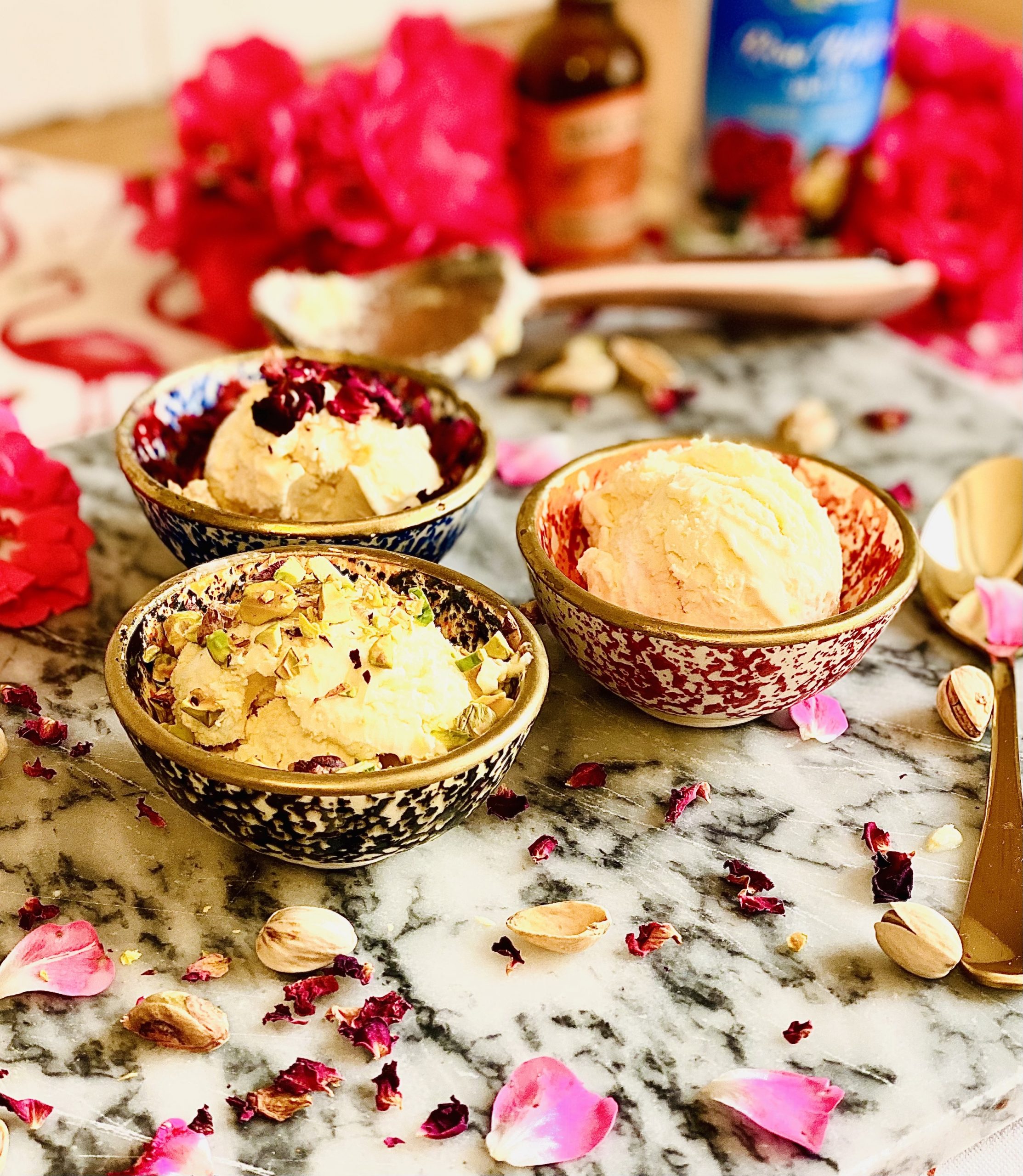 Scoops of Turkish Delight no churn ice cream, scooped into three small bowls, with crushed pistachios and rose petals topping the dessert. Surrounded on a table by roses and an ice cream scoop.