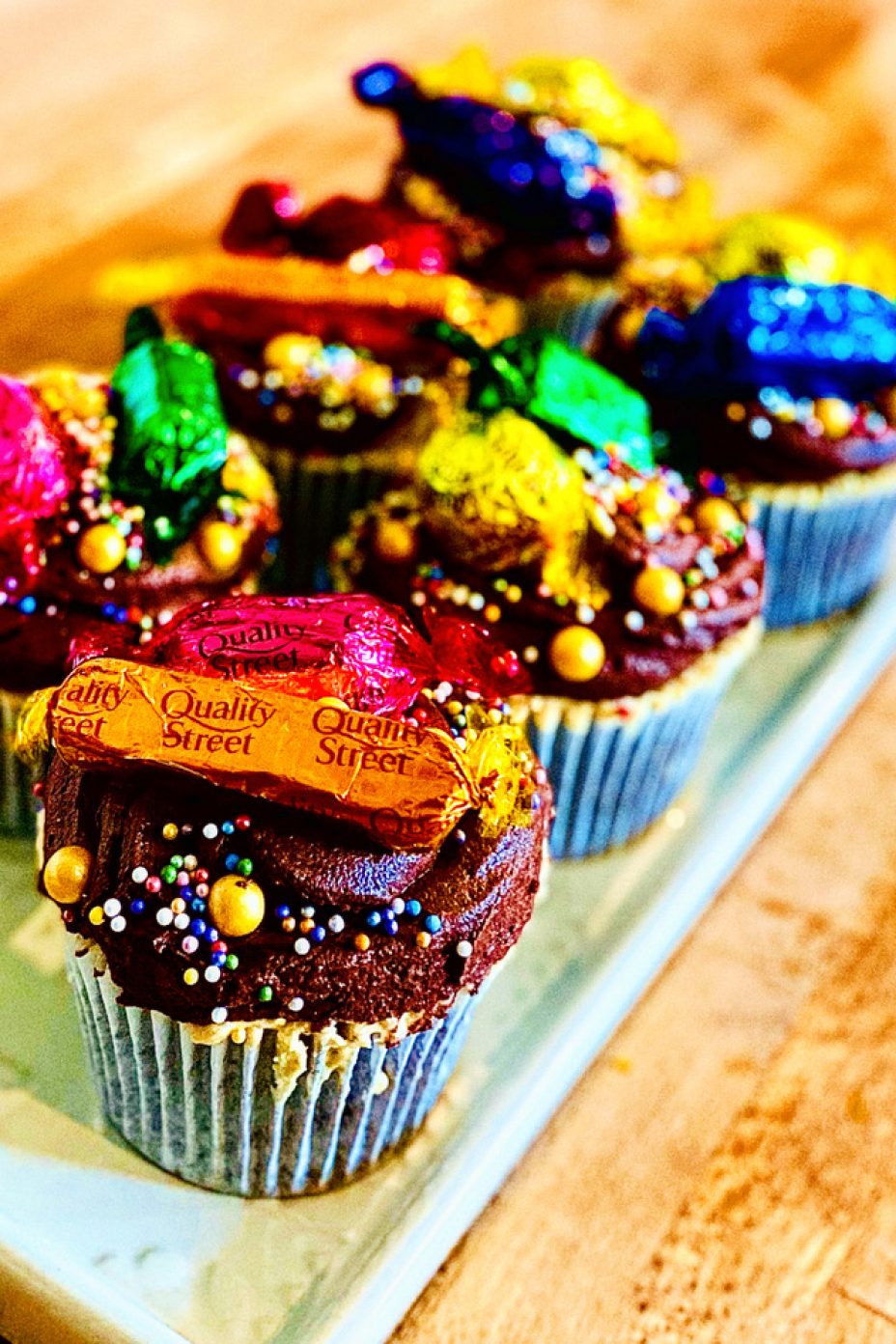 6 chocolate and dulce de leche cupcakes with chocolate icing and topped with a variety of Quality Street chocolates and gold sprinkles