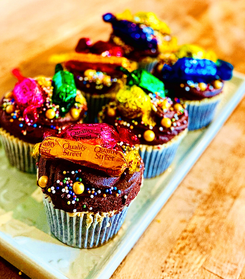 6 chocolate and dulce de leche cupcakes with chocolate icing and topped with a variety of Quality Street chocolates and gold sprinkles