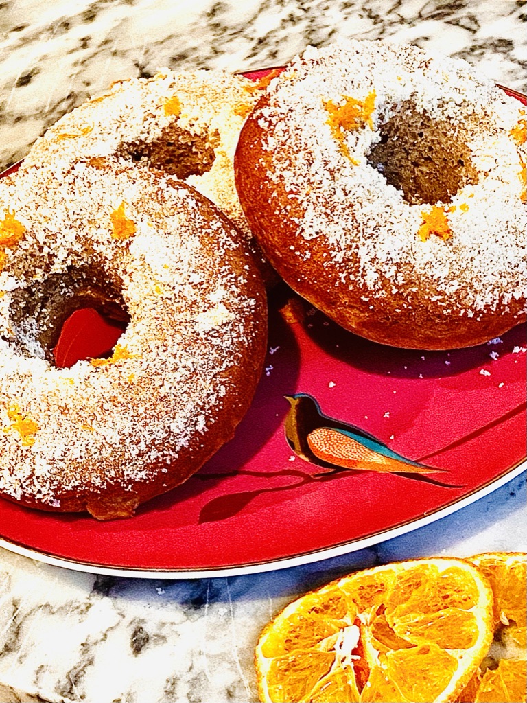 Baked banana and cinnamon breakfast doughnuts with orange sugar. Displayed on a plate with orange slices below for decoration.