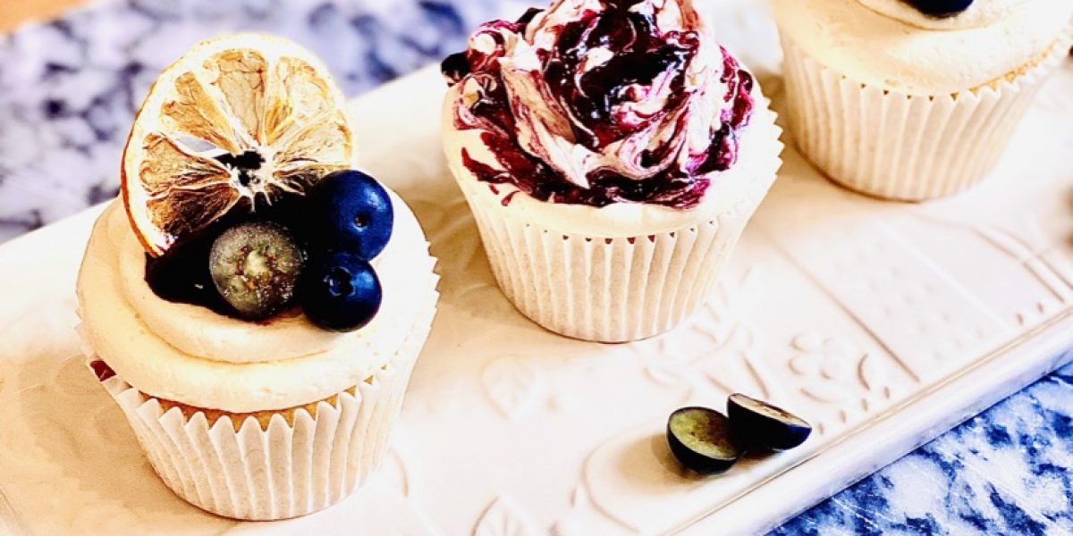 Three lemon and blueberry cupcakes decorated with blueberry jam, lemon slices and fresh blueberries