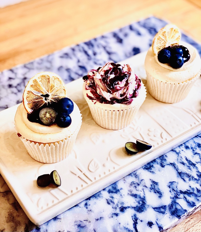Three lemon and blueberry cupcakes decorated with blueberry jam, lemon slices and fresh blueberries